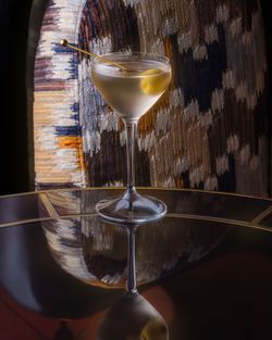 Martini glass with an olive garnish placed on a reflective table surface in a restaurant setting.