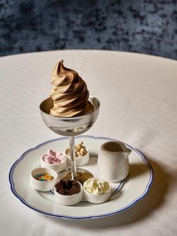 Chocolate soft serve served with various toppings and a small jug of sauce on a white plate at La Tête d'Or by Daniel.