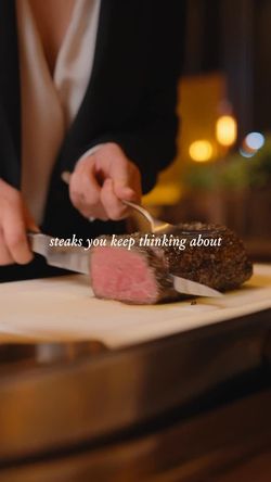 Person slicing a medium-rare steak on a wooden board at a steakhouse restaurant.