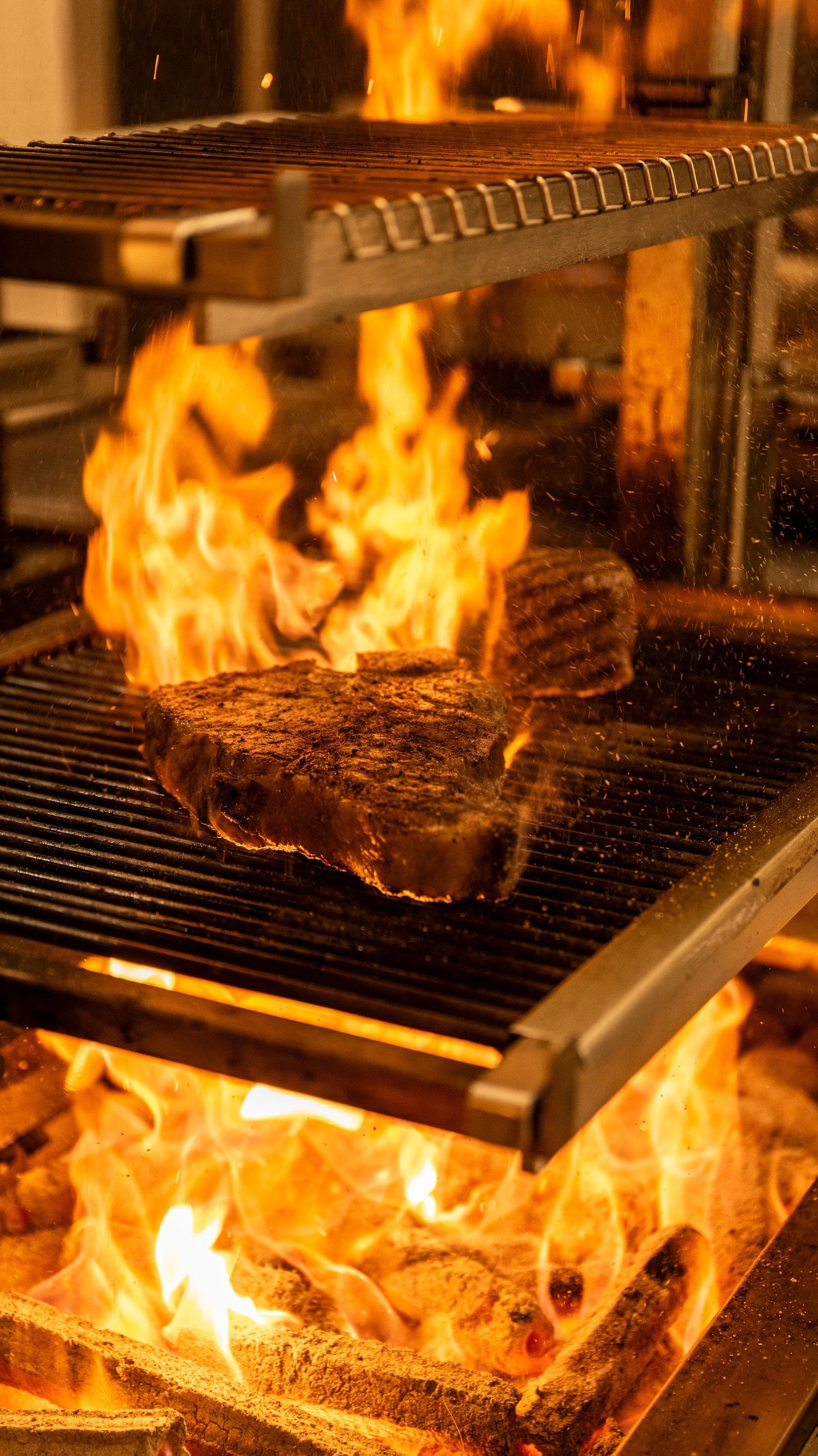 Flames engulf a steak sizzling on a grill, showcasing a vibrant cooking process at La Tête d'Or.