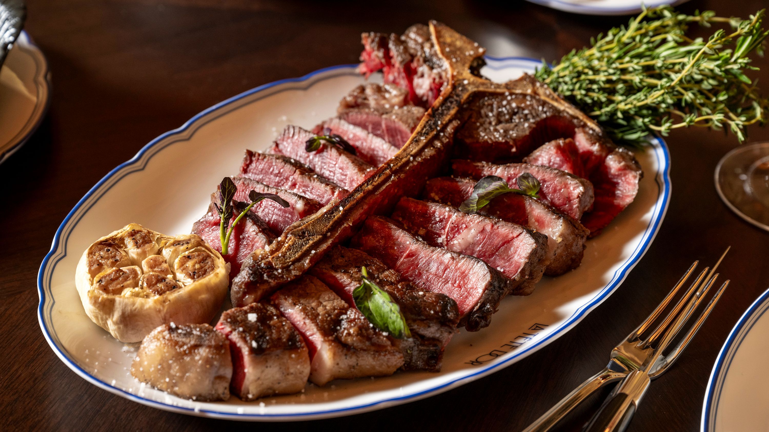 Sliced prime rib presented on a platter, garnished with herbs and roasted garlic, served at La Tête d'Or.