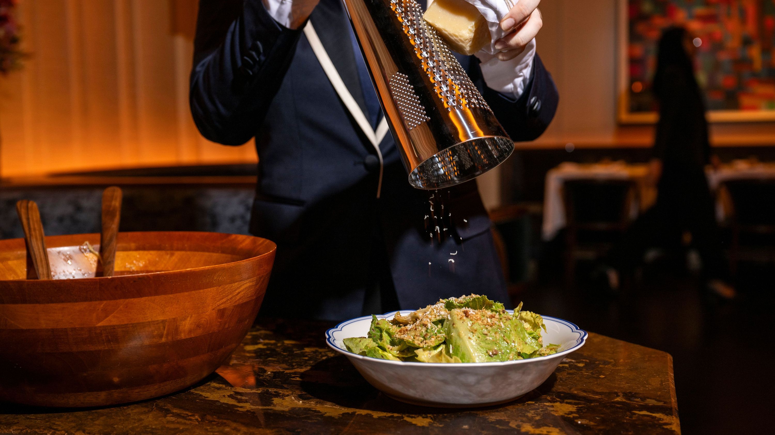 A server grates cheese onto a fresh, vibrant salad, showcased at La Tête d'Or by Daniel in NYC.
